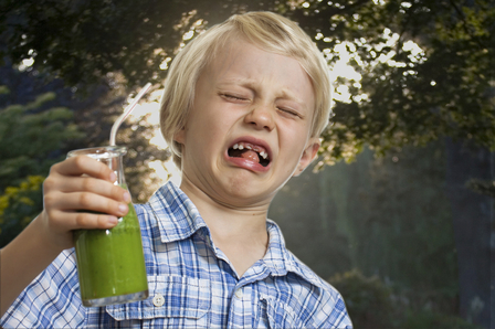 A young boy looking very disgusted holding a green smoothie. Isolated on white.